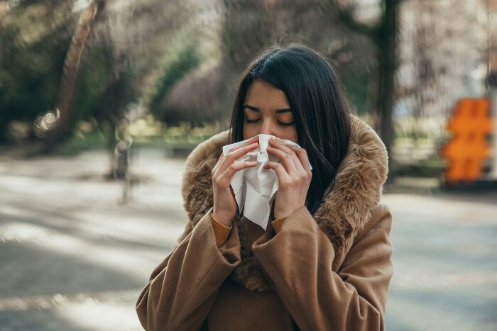 Traveler sneezing outdoors, wrapped in a warm coat, illustrating an awkward travel moment.