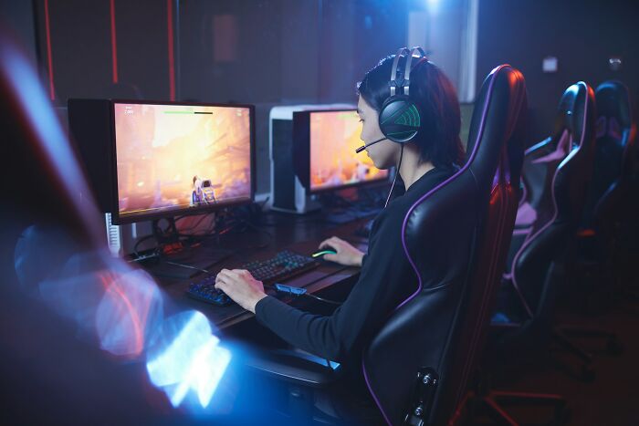 Person with headset playing video games at a computer, highlighting a fun job that might be less enjoyable than expected.