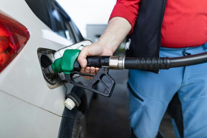 Traveler refueling car at gas station in blue pants and red shirt, illustrating cringeworthy travel situations.