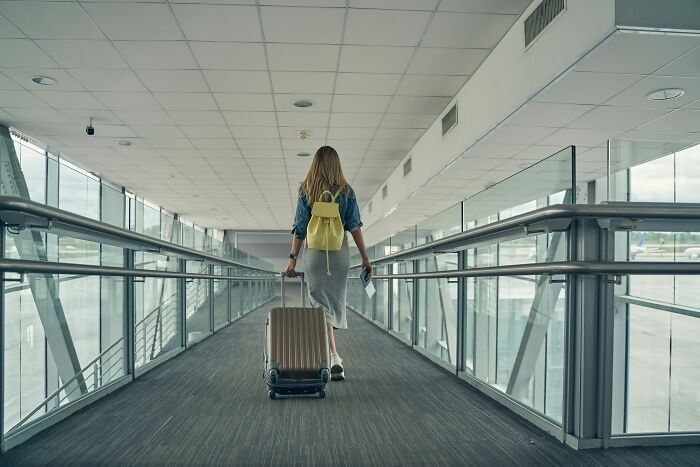 Person with a yellow backpack and suitcase walking through an airport corridor, experiencing an astonishing coincidence.