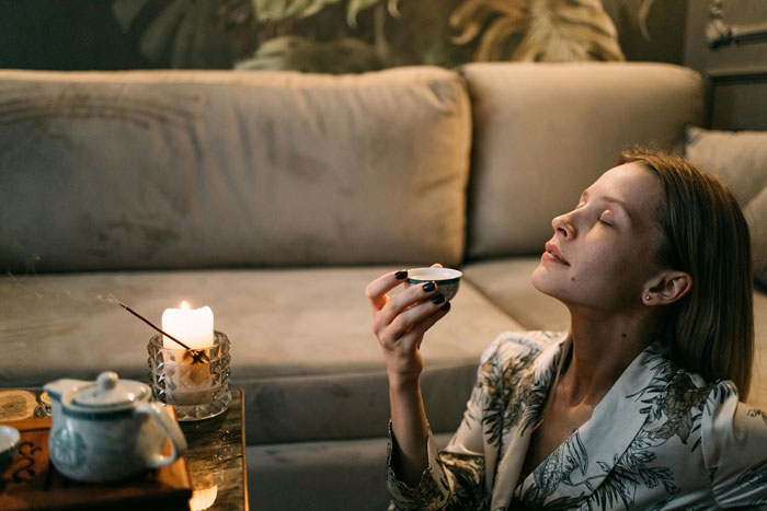 Woman enjoying a moment with incense and tea in a cozy living room