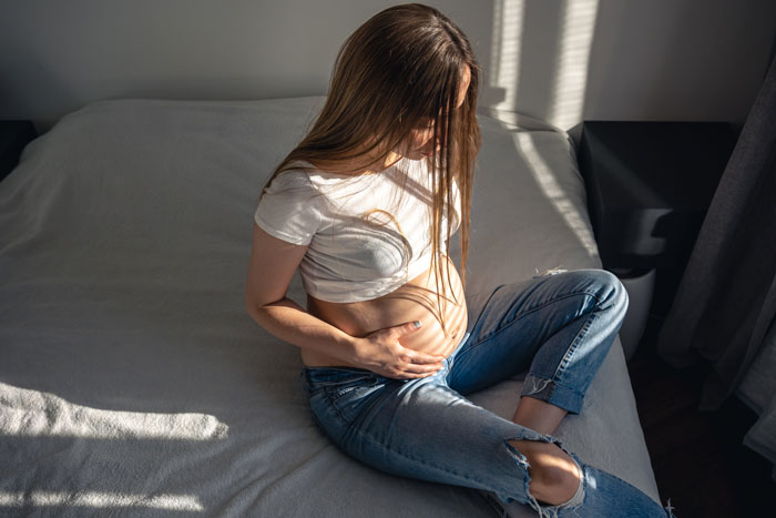 Woman sitting on bed, holding her baby bump, symbolizing 