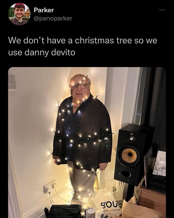 Cardboard cutout of a man wrapped in Christmas lights, standing next to speakers and bags, showcasing a funny meme.