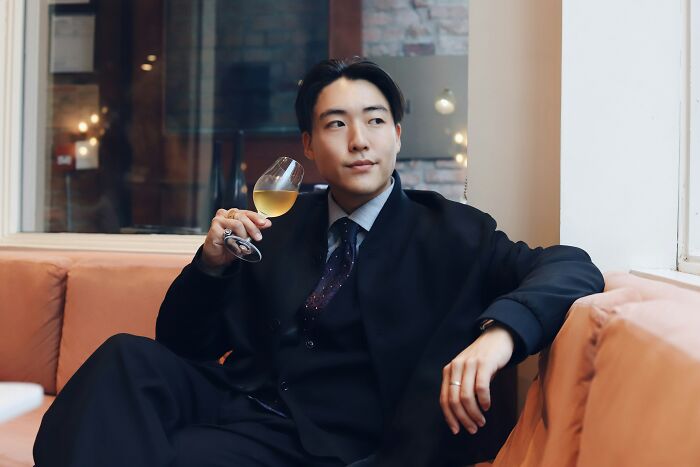 Young man in upscale setting, holding wine glass, embodying lifestyle of rich kids oblivious to the real world.