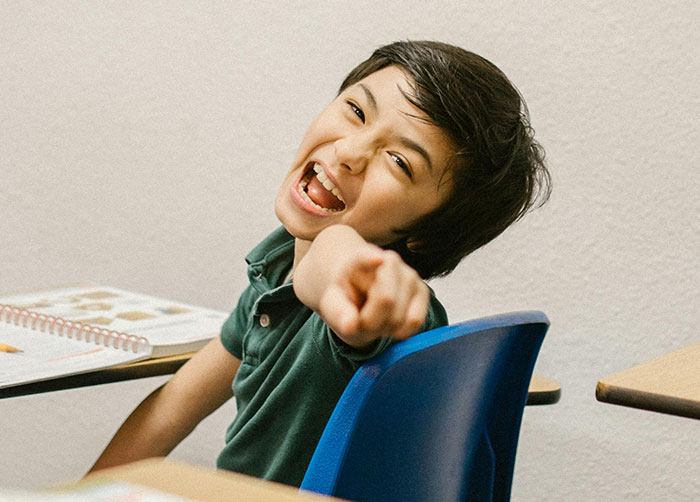 Child pointing and laughing disruptively in a classroom setting, illustrating a bully's behavior.