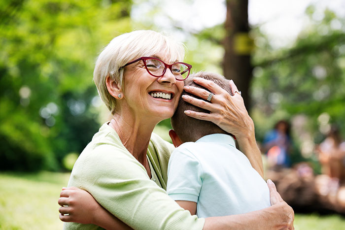 Grandma hugs boy in park, smiling courageously, preventing bullying incident.