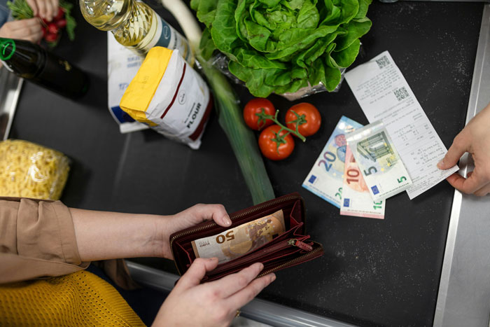 Arctic grocery cost: wallet with money, receipt, fresh produce on checkout counter.