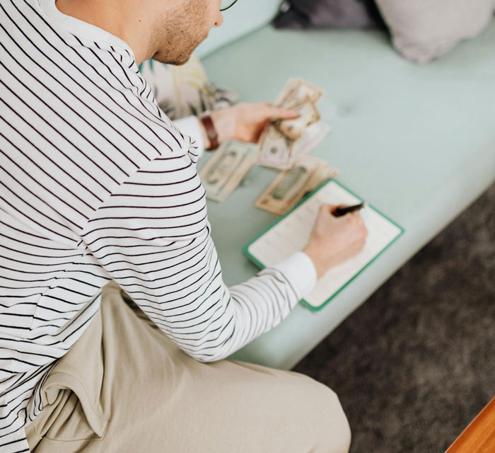 Man in striped shirt counting money, writing in notebook, highlighting cost concerns for a destination wedding.