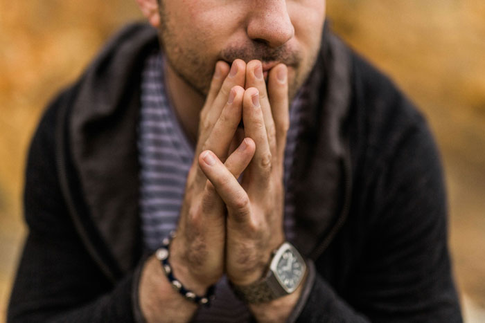 Groomsman looking concerned, resting his chin on hands, contemplating destination wedding expenses.