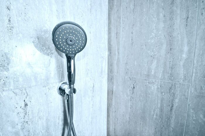 Shiny shower head against gray tiles, showcasing a frugal home hack for a luxurious bathroom experience.