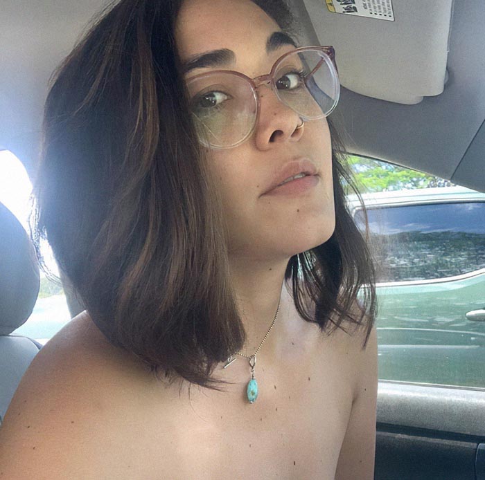 A woman with glasses and short hair sits in a car, wearing a gemstone necklace, focusing on her healing journey.