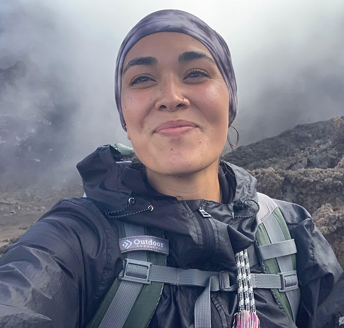 Woman in outdoor gear amidst misty rocky landscape, focused on healing journey.