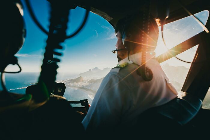 Pilot flying helicopter over coastal landscape, illustrating professions viewed as relationship red flags.