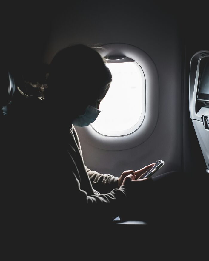 Person on a plane, silhouetted against the window light, using a phone; relating to professions and relationship red flags.