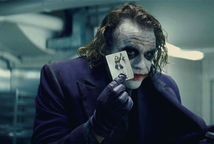 A character in makeup and a purple coat holds a joker card, illustrating popular themes in fascinating fan theories.