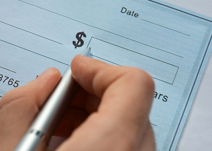 Hand writing a check, symbolizing HOA's financial disputes over alleged violations.