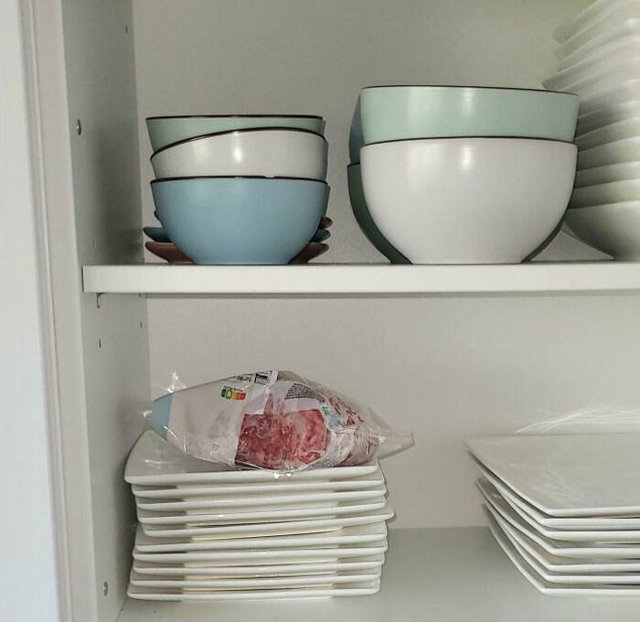 Frozen meat stored in a kitchen cabinet with bowls and plates, illustrating a situation with horrible roommates.