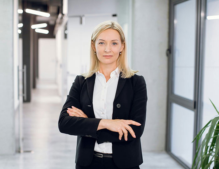 HR professional in office attire stands confidently in a modern workplace setting.