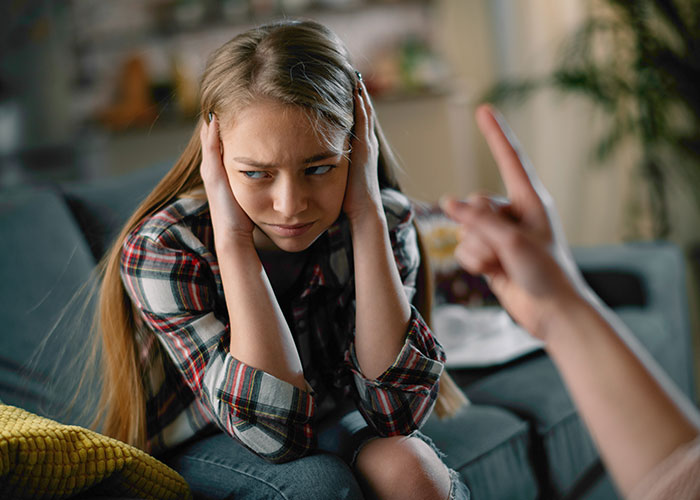 Teen girl covering ears during a discussion about her behavior towards baby.