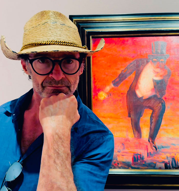 Mysterious man in glasses and straw hat poses near vibrant painting.