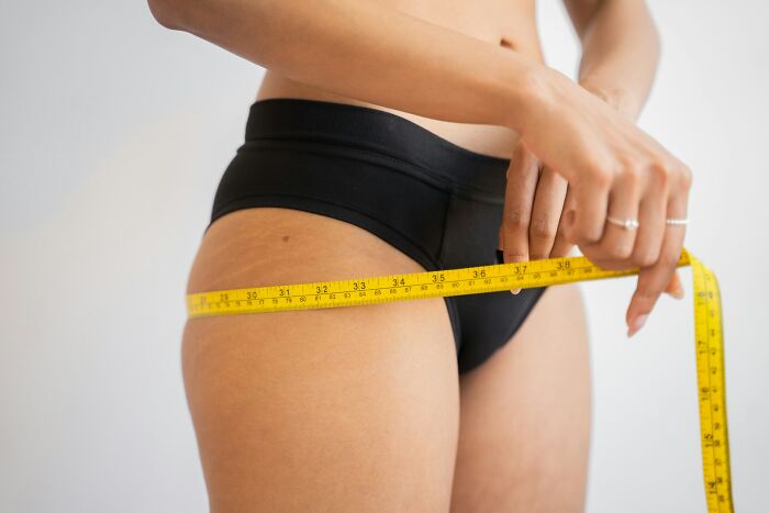 Person measuring hips with tape, illustrating exercise's impact on body shape.