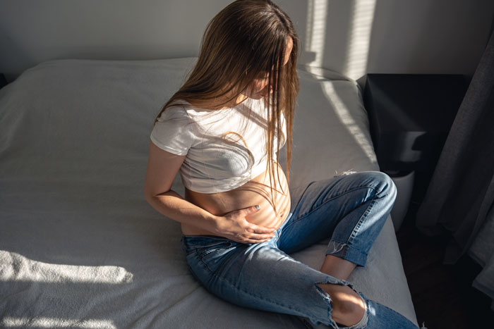 Pregnant woman sitting on a bed, holding her belly, contemplating baby names.