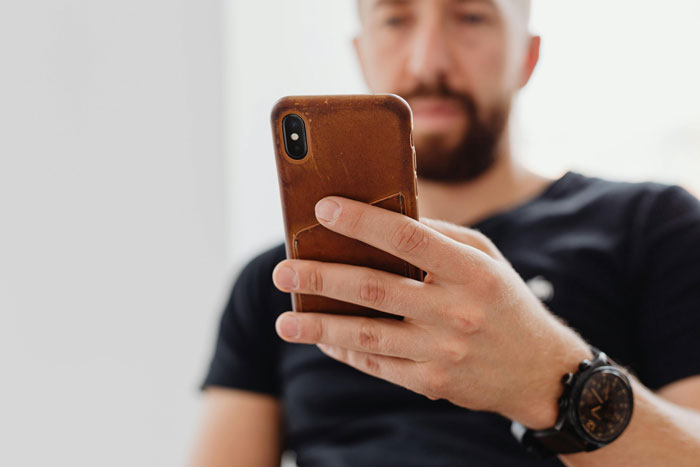 Man holding a smartphone, focusing intently, set in a casual atmosphere.