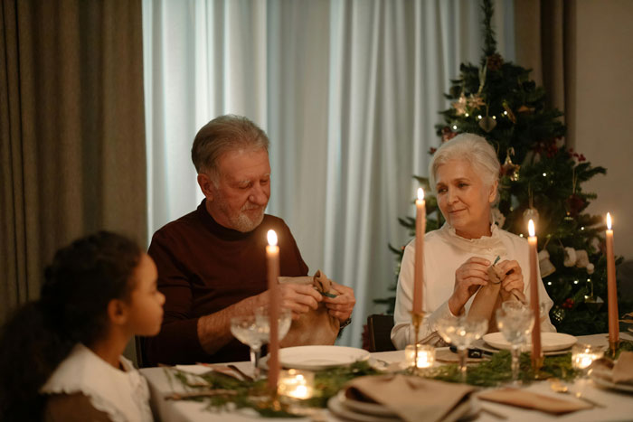 Family enjoying Christmas dinner with husband, wife, and child at a festive table near a decorated tree.