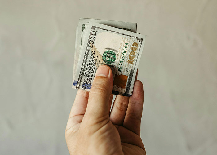 Hand holding hundred-dollar bills, symbolizing a budget challenge for Christmas planning.