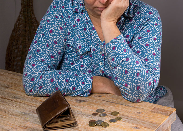 Woman in a patterned shirt sitting at a table with coins and an open wallet, appearing thoughtful.