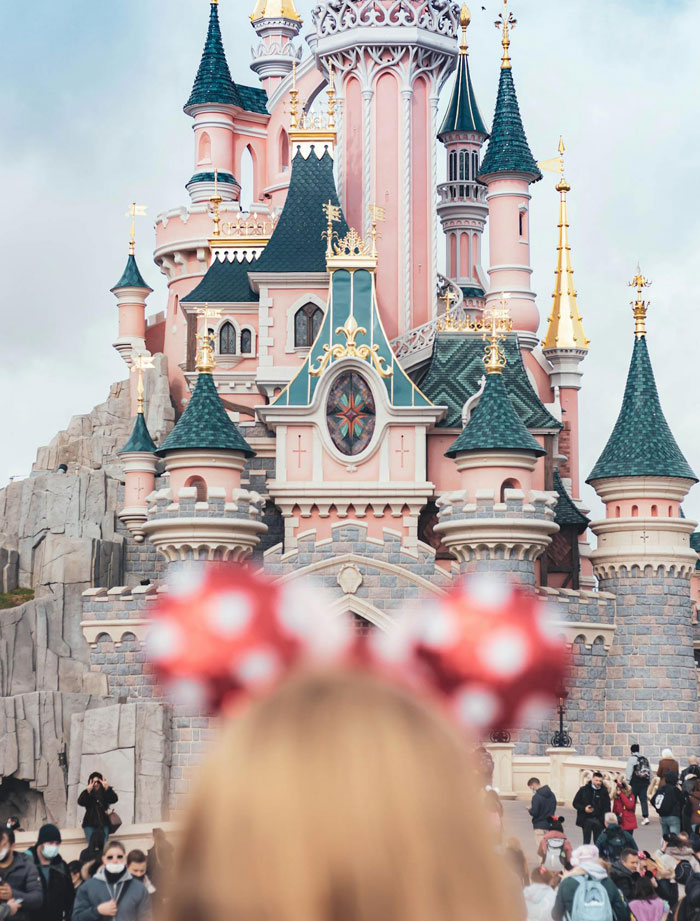 Disney castle with a crowd in the foreground, featuring a person wearing Mickey Mouse ears, illustrating frequent theme park visits.