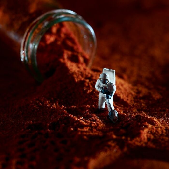 Miniature astronaut with a spoon in a pile of paprika, showcasing the tiny world of foods created by a creative duo.