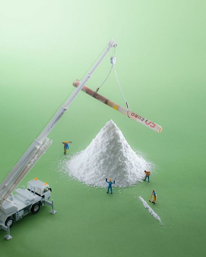 Miniature scene with tiny figures and a crane lifting a rolled euro bill over a white powder mound, showcasing creative miniatures.