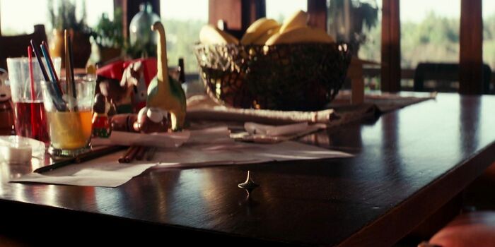 Spinning top on a table, surrounded by colorful pencils and a fruit bowl, sparking fascinating fan theories.