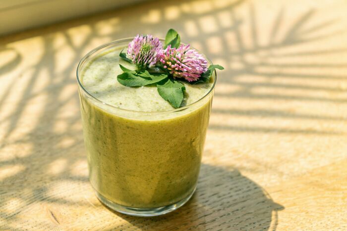 Green smoothie in a glass with clover garnish on a sunlit wooden table, representing industries built on deception.