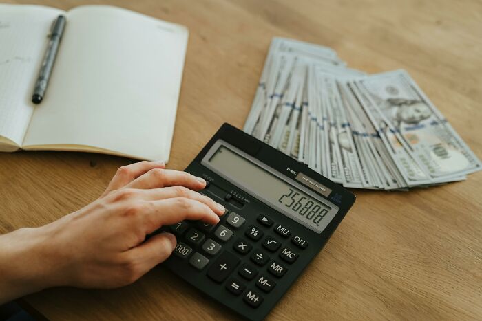 Person using a calculator with cash and a notebook nearby, symbolizing industries built on deception.