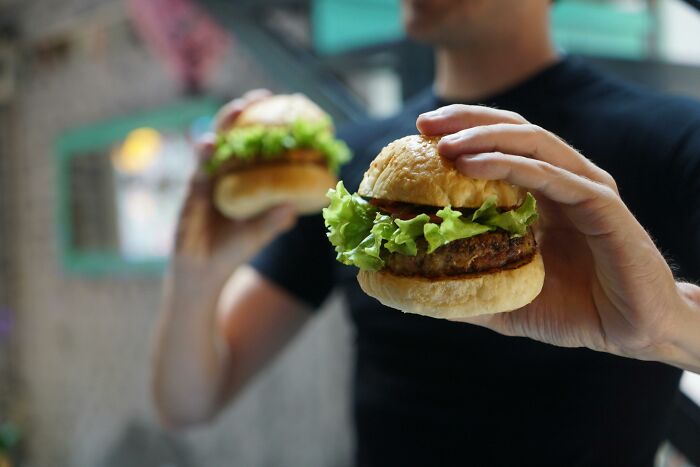 Person holding two burgers with lettuce, highlighting the food industry.