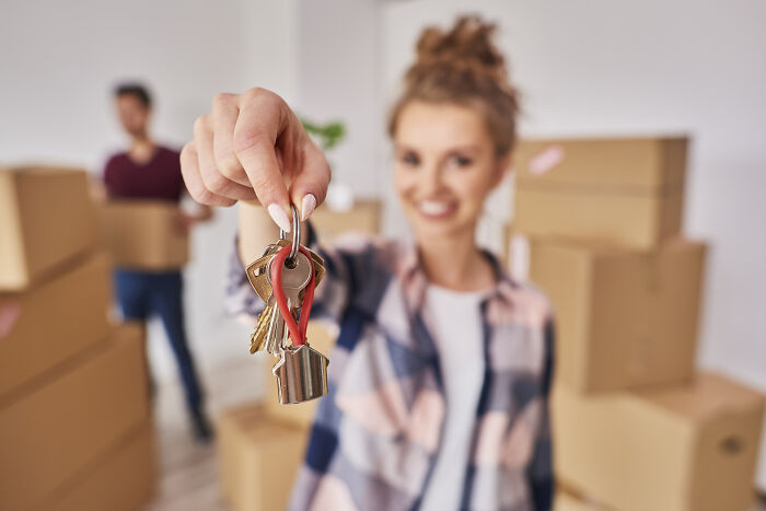 A woman holding keys with moving boxes in the background, highlighting the theme of deceptive industries.