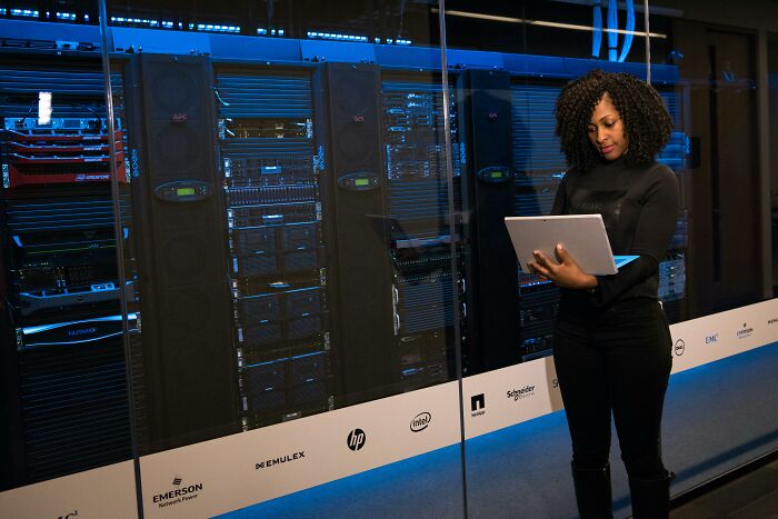 Woman holding a laptop in a server room, highlighting industries built on deception.