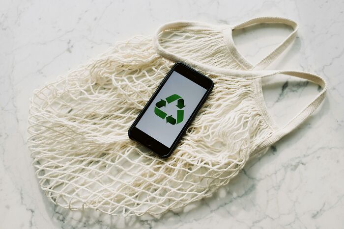 Smartphone with recycling symbol on mesh bag, hinting at industries founded on deception.