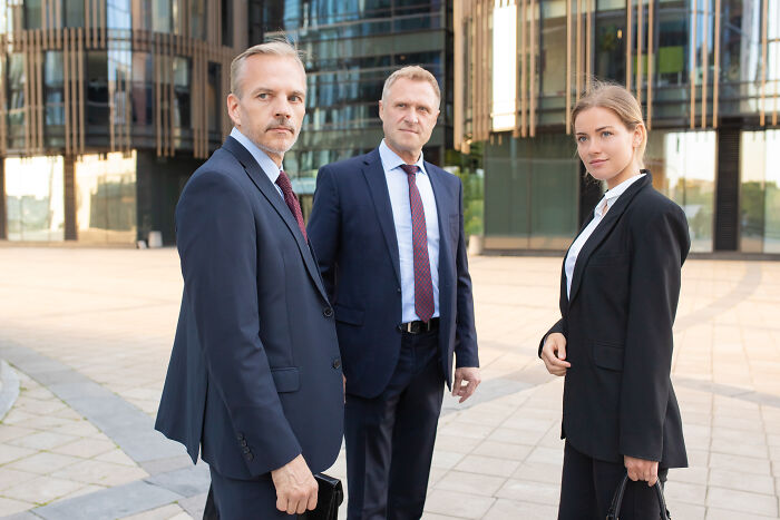 Three business professionals in suits standing outside an office building, related to industries fooling people.