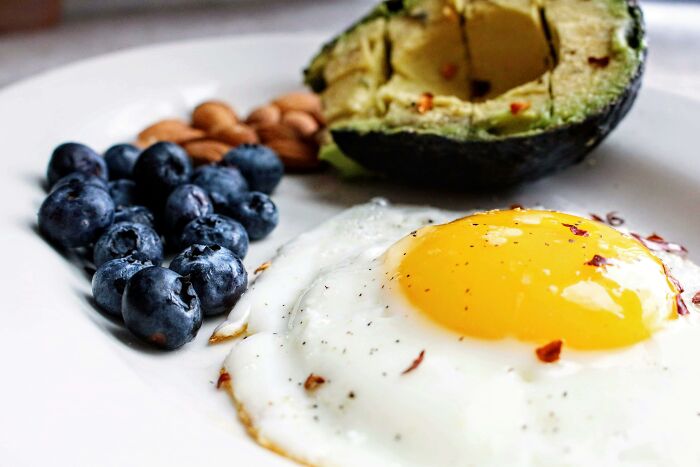 Avocado, almonds, blueberries, and a sunny-side-up egg arranged on a white plate.