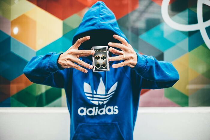 Person in blue Adidas hoodie performing card tricks, suggesting deceptive foundations in certain industries.