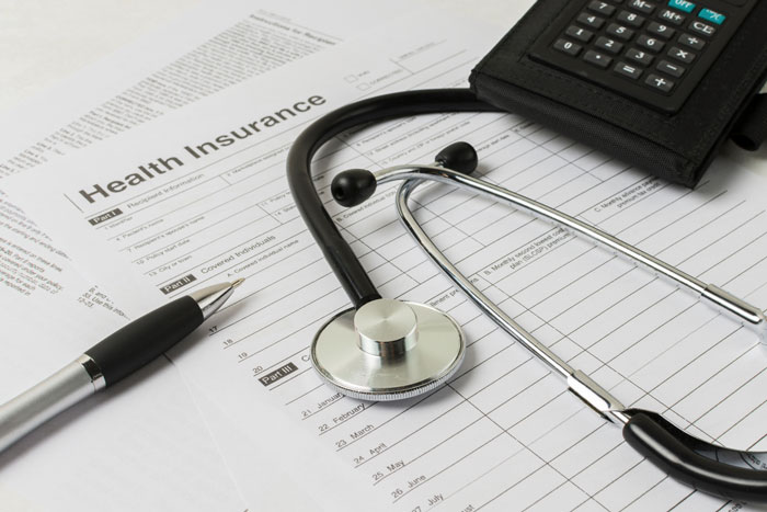 Stethoscope on health insurance form with pen and calculator, highlighting insane hospital bill concepts.