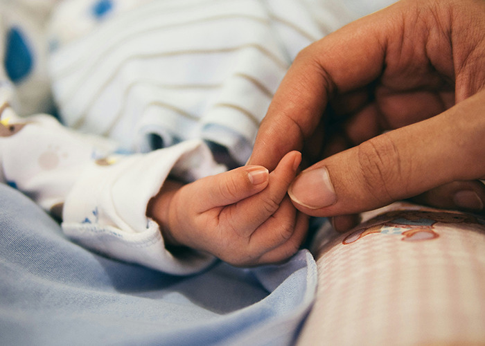 Adult hand gently holding a baby's hand, symbolizing trust amidst real-life insurance challenges.