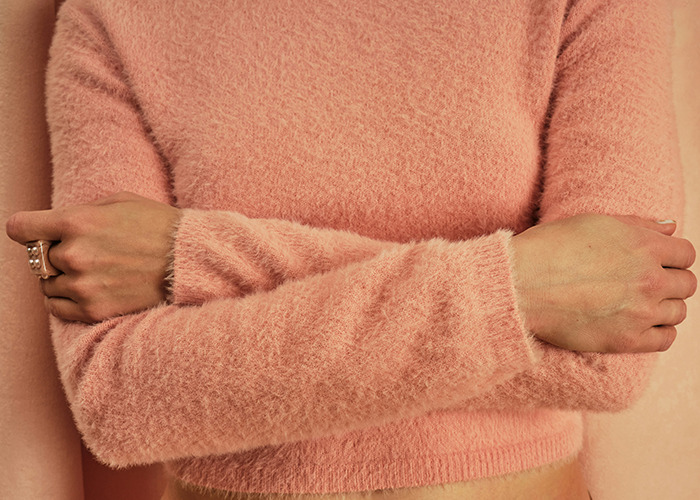 Person in a pink fuzzy sweater with crossed arms, representing frustration, related to insurance horror stories.