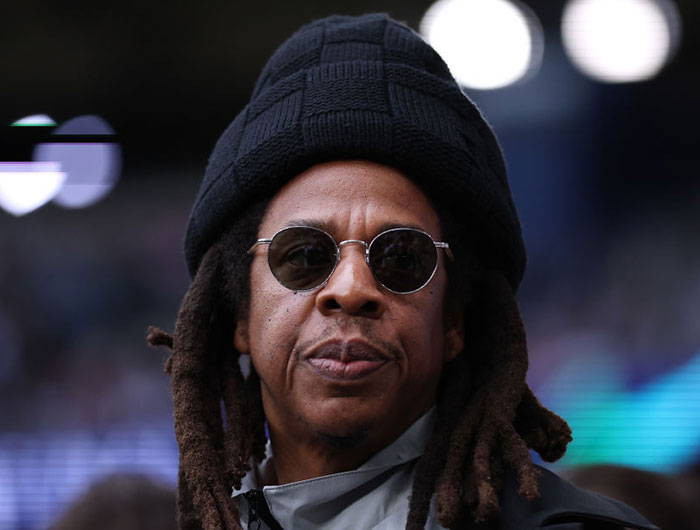 Rapper Jay Z in sunglasses and hat, associated with assault accusation, looking serious.