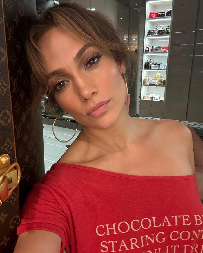 Jennifer Lopez in a stylish red top with gold hoop earrings poses indoors, emphasizing a chic, modern look.