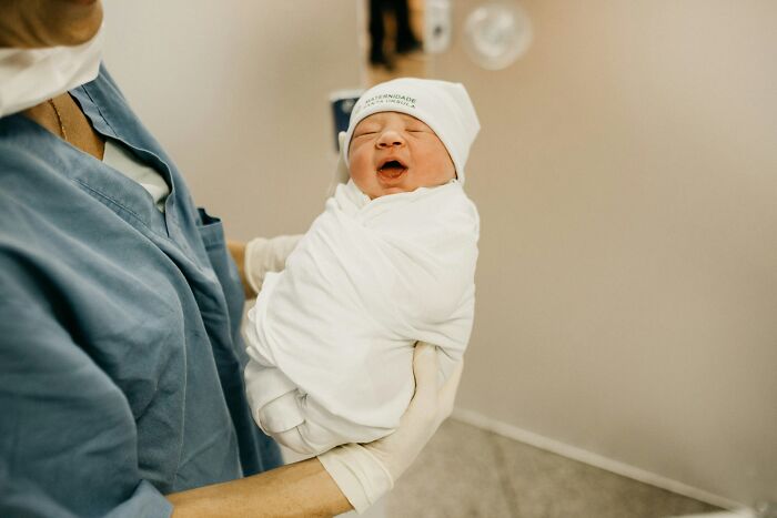 A newborn baby wrapped in a blanket, held by a nurse, showcasing an astonishing coincidence.