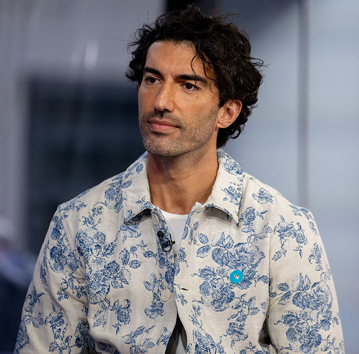 Man in a floral shirt appears thoughtful while sitting during an interview, focused on lawyer claims related to Justin Baldoni.